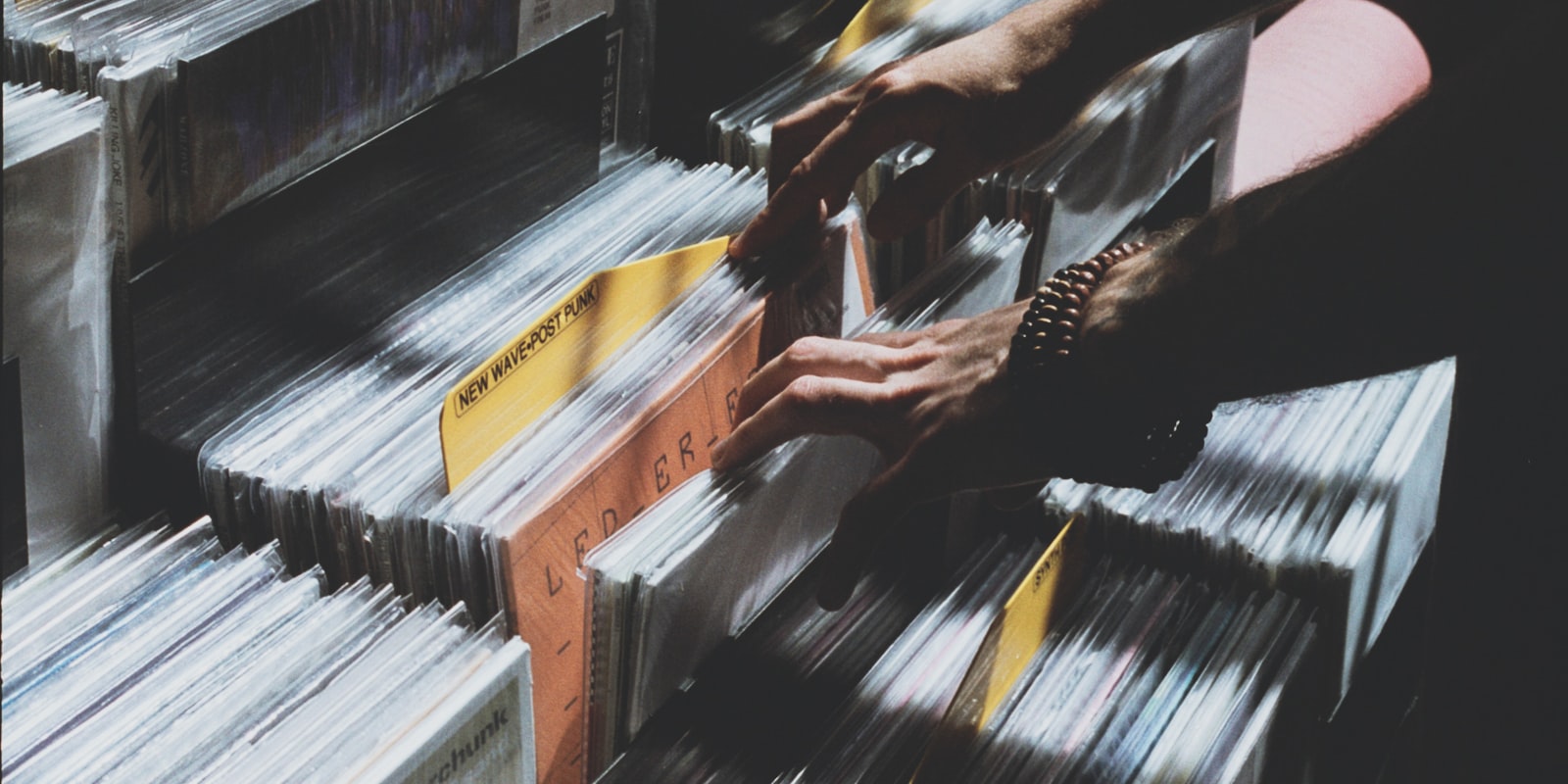 Hands flipping through vinyl records in a record store bin